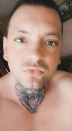 A shirtless man with a goatee and a neck tattoo looks up.