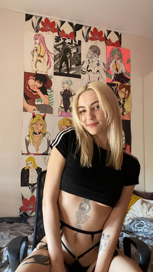 Slim blonde in black crop top and strappy lingerie poses in bedroom with anime posters.