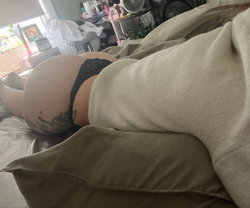 Person with tattoos lying on a bed in a cluttered room.