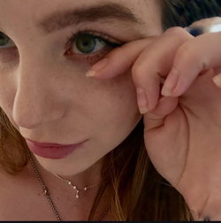 Woman with green eyes and blonde hair adjusts her face near a phone.