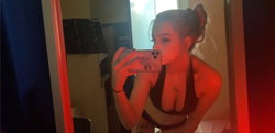 A woman with dark hair in a bun takes a selfie in a red-lit room.