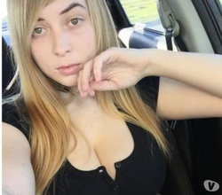 Blonde woman with long hair in a black top, sitting in a car, resting hand near chin.