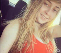 Blonde woman in a red top smiling in a car.