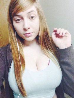 A young woman with long blonde hair and a light top poses in a casual setting.