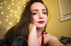 Brunette woman with long hair and red lipstick, wearing a red halter top, resting on a bed with string lights in the
