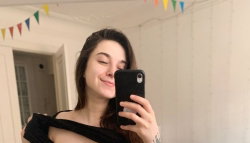 A young woman with long brown hair takes a selfie in a room with colorful bunting.