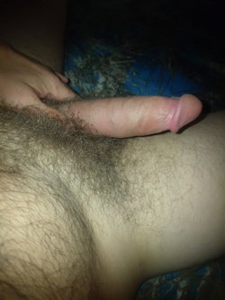 Close-up of a man's erect penis being held, with pubic hair visible and a dark patterned fabric in the background.