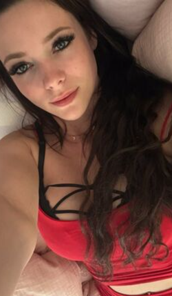 Brunette woman with long dark hair lying down, wearing a red and black strappy top, looking at the camera in a close-up
