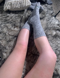 Person in gray socks and beige skirt lounges on a fluffy gray blanket.