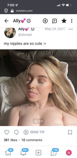Blonde woman lying on a bed, topless, with closed eyes and tongue out, wearing a delicate necklace.