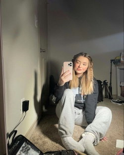 Blonde woman in casual clothes taking a selfie in a bedroom.