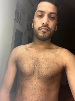 Shirtless man with dark hair and beard takes a selfie indoors showing his chest.