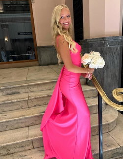 Blonde woman in a bright pink satin gown poses on marble stairs, holding white flowers, with a small heart tattoo on