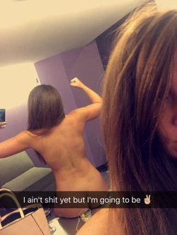 A woman with long hair poses topless in a bathroom.