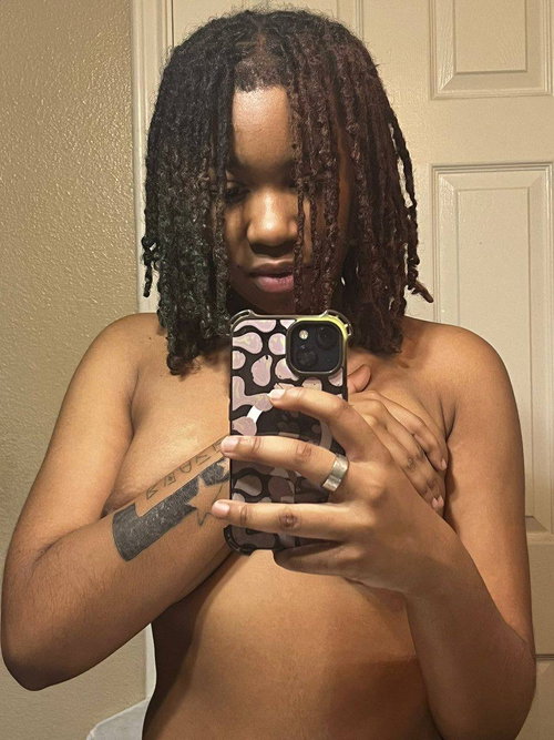 Ebony woman with dreadlocks takes selfie in bathroom, arms covering chest.