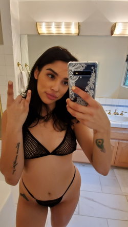 Woman in black lingerie taking a selfie in a bathroom with gold fixtures.