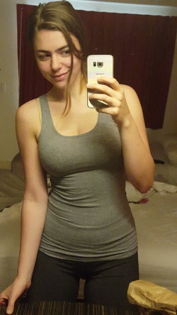 A woman with long brown hair takes a selfie in a gray dress.