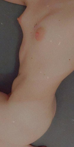Close-up of a person's bare chest and upper torso, showing skin with freckles and a visible nipple, lying on a dark