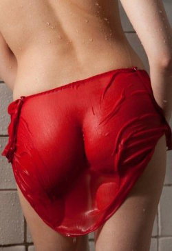 A person with a curvy build wearing red satin thong-style underwear, standing in a tiled shower with water droplets on
