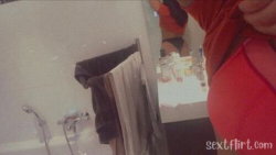 A person in a red top and dark underwear stands in a bathroom, partially visible with a mirror reflecting their lower
