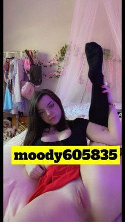 A woman with long dark hair lies on a bed in a bedroom, wearing a black top and red skirt, lifting one leg in black