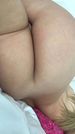 Close-up of a person's bare buttocks and lower back, lying on a white surface with pink fabric visible near the waist.