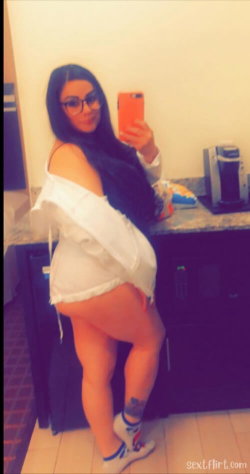A woman with long dark hair and glasses takes a mirror selfie in a white off-shoulder top, showing her legs and a