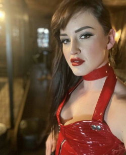 Brunette woman in a red latex halter top with choker, posing indoors with dramatic makeup and styled hair.