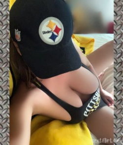 Woman in black sports bra and Pittsburgh Steelers cap, lying on yellow fabric with arm visible, suggesting a selfie