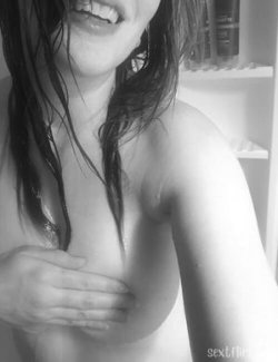 Close-up of a woman with wet dark hair, partially covering her bare chest, hand resting on her breast in a bathroom