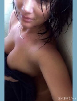 Brunette woman with wet hair, bare shoulders, wearing a delicate necklace, partially wrapped in a dark towel against a