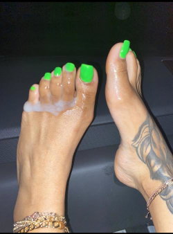 Close-up of feet with bright green toenails, one foot showing a tattoo on the ankle and both adorned with bracelets,