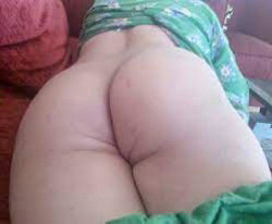 Close-up of a person's bare buttocks with green floral fabric wrapped around the waist, sitting on a red couch.