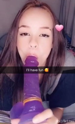 Woman with long hair holds a purple toy, smiling in a bedroom setting.