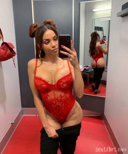 Woman in red lace bodysuit and black pants poses in mirror selfie, pulling down pants to expose underwear, in a room