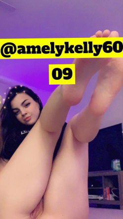 Brunette woman with curvy build lying down, legs raised, wearing black top, in a room with purple lighting.