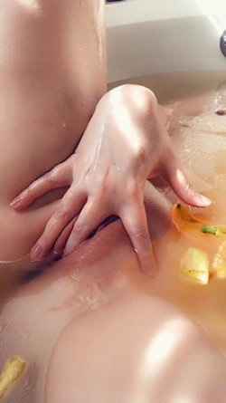 Close-up of a person's wet torso and hand in a bathtub with floating flower petals, partially submerged in water.