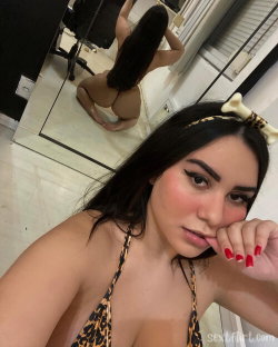 Brunette woman in leopard print top takes selfie, reflection shows her kneeling in mirror, wearing matching headband.