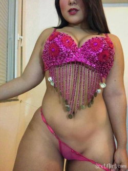 Curvy woman in a pink beaded top with fringe and matching thong, posing indoors near a window.