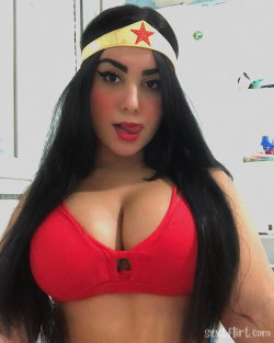 Brunette woman with long hair wearing a red bra and Wonder Woman headband, posing indoors in a selfie-style shot.