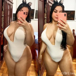 Brunette woman in a white one-piece swimsuit with bunny ears, taking mirror selfies in a bedroom setting.