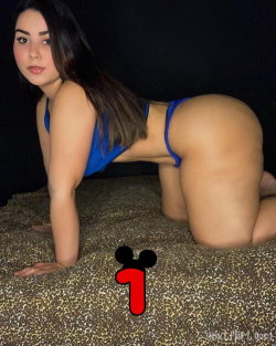 Brunette woman with curvy figure in blue lingerie posing on a leopard-print surface against a dark background.