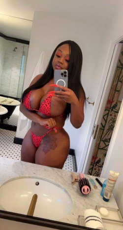 A curvy woman with long dark hair takes a mirror selfie in a red polka-dot bikini, standing in a bathroom with a