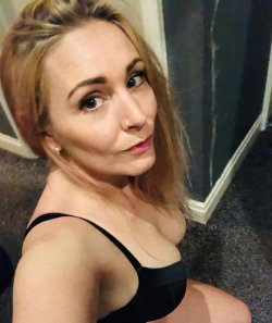 Blonde woman with a curvy figure wearing a black bra, posing indoors in a selfie-style shot.