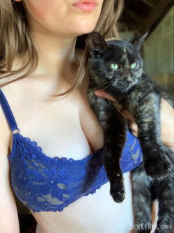 Woman with shoulder-length hair wearing a blue lace bra, holding a black cat close to her chest in an indoor setting.