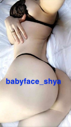 Curvy woman lying on white bedding, wearing black lace bra and thong, hand resting on hip.