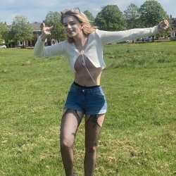 Blonde woman in a white top and denim shorts poses in a park.