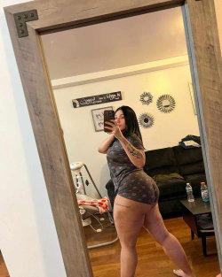 A woman in a floral short outfit poses in front of a mirror, taking a selfie.