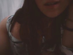 Close-up of a woman with long dark hair wearing a patterned tank top, partially visible in dim lighting.