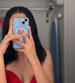 Woman with long dark hair in red strapless top takes mirror selfie, phone covering face, in closet setting.